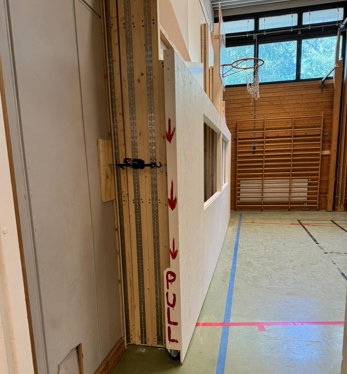 The photo shows a folded squash court in a gym. The court is compactly stored against the wall, with the wooden structure clearly visible.