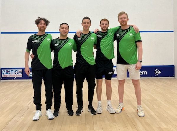 The image shows a group of five male squash coaches standing together on a squash court