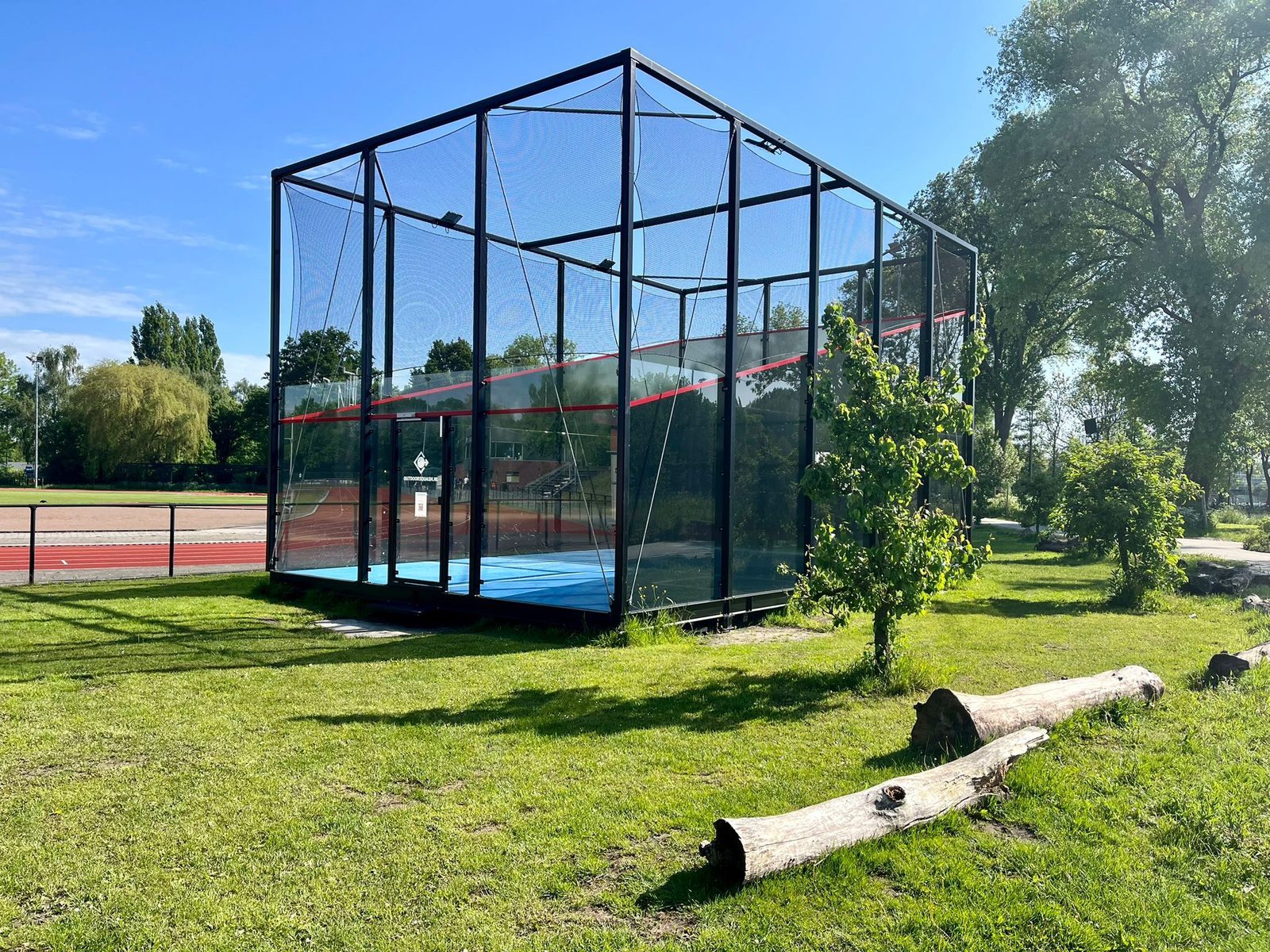 The court is enclosed by tall metal frames and fine mesh netting, enhancing ball retention and safety for players.