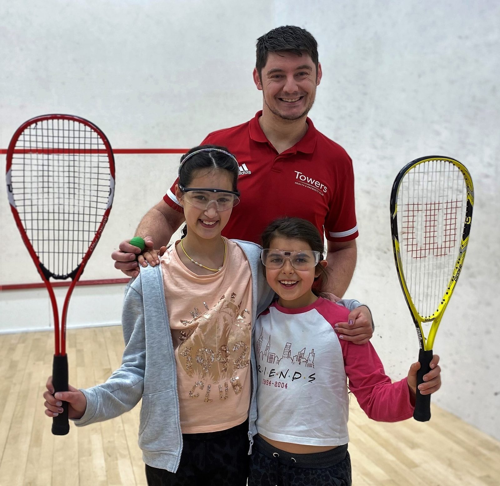 Photo is showiung a coach with a girl holding a Squash rachet and another girl holding a Squash 57 racket