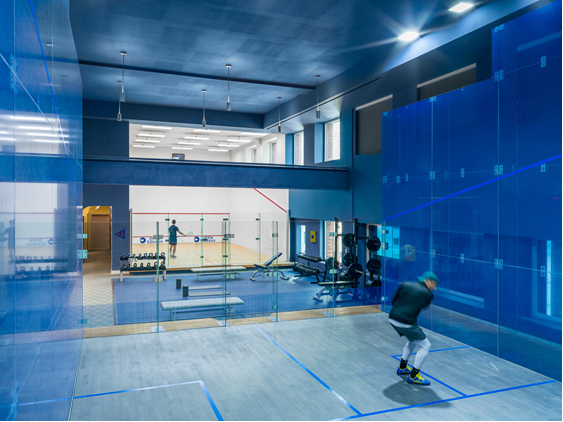 Modern squash facility with a blue glass court, visible weight training area, and multiple courts in view at Open Squash FiDi.
