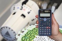 The image shows a thermostat in the background, a hand holding a scientific calculator in the foreground, and a stack of euro banknotes. It likely conveys a concept related to calculating or managing heating costs or energy savings.